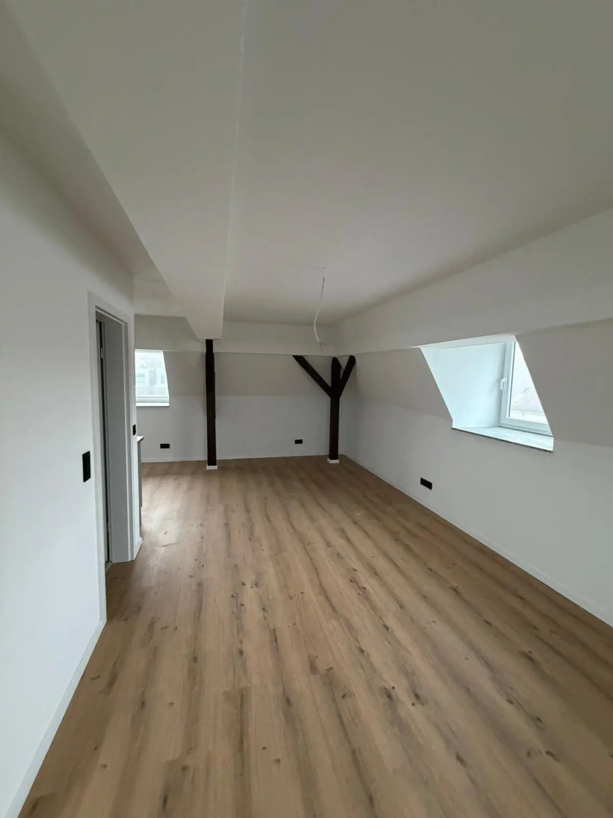 Augsburg, Hauptfläche des Dachgeschosses nach dem Ausbau: heller Wohnraum mit Dachfenstern, sichtbarem Holzbalken und Boden in Holzoptik