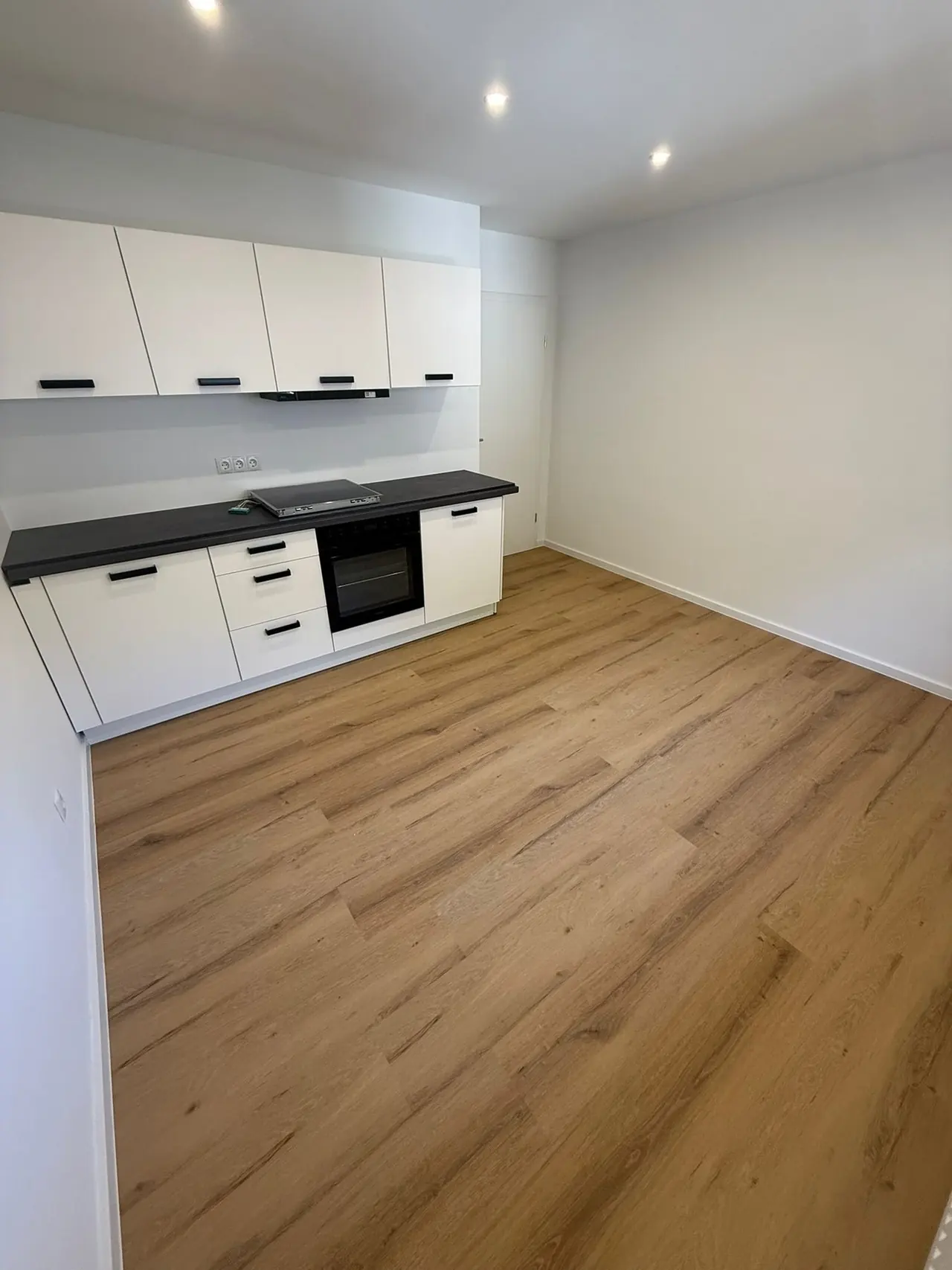 München, Wohnküche nach der Kernsanierung: weiße Küchenzeile mit schwarzer Arbeitsplatte und Boden in Holzoptik