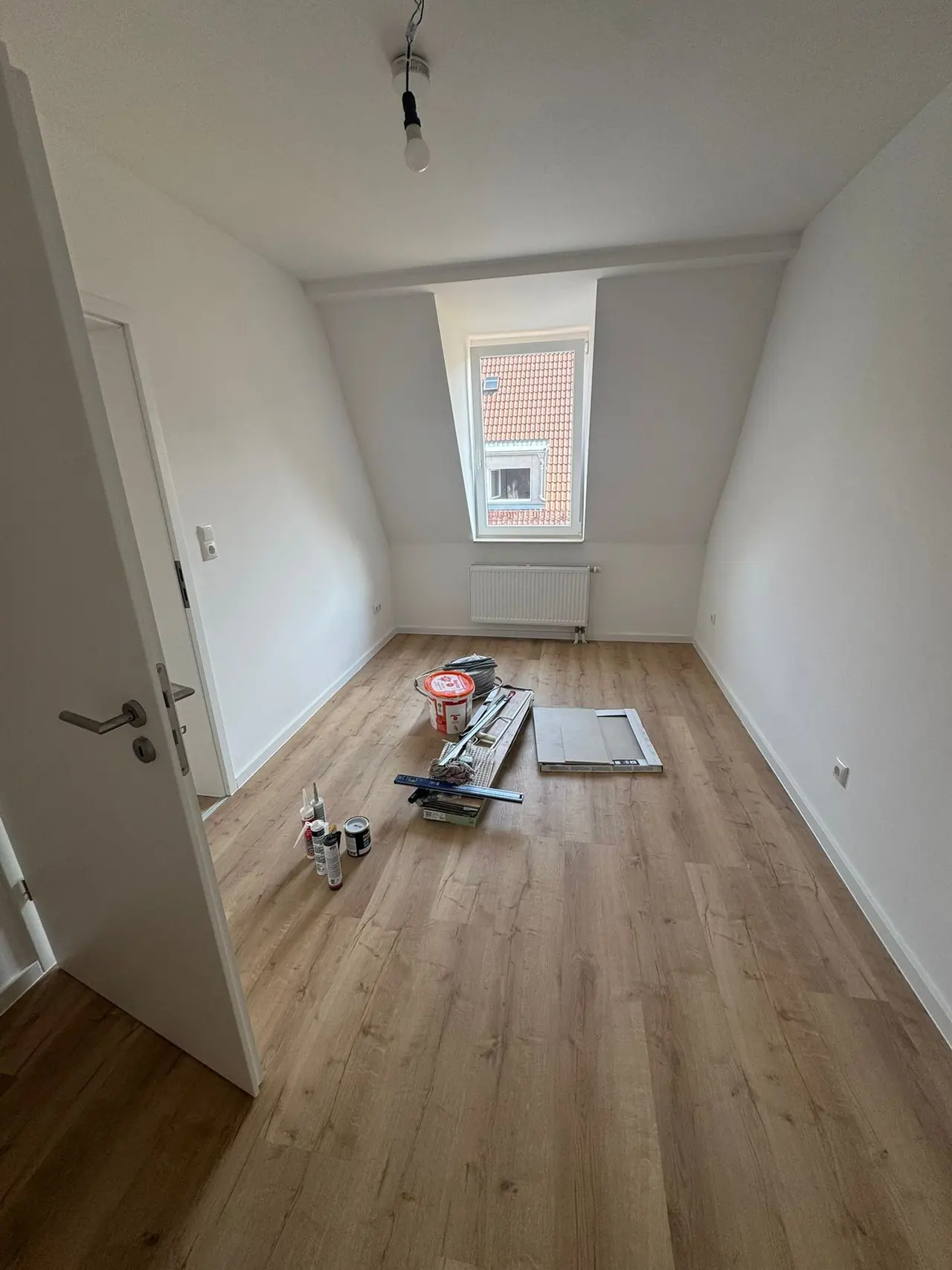Nürnberg, Zimmer nach der Sanierung: heller Raum mit Dachfenster und warmem Holzdekor-Boden
